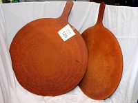 Photo showing two round wooden pizza serving trays side by side on a white cloth background, highlighting their size difference and shape with handles.