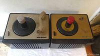 Two vintage RCA Bakelite turntables with different colored tops and control knobs, placed side by side on a white cloth surface
