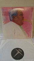 Front view of the album cover showing an illustrated portrait of Charlie Parker playing the saxophone in warm colors with a pink background. Visible is one black vinyl record with the Verve label.