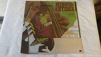 Front cover of Mingus at Antibes double album, colorful illustration of Charles Mingus with bass, album title and credits visible.