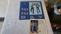 Two vinyl record singles by Paul McCartney and Michael Jackson, one with a blue cover titled 'Say Say Say', and the other a white sleeve for 'The Girl is Mine'. Both records are in good visual condition.