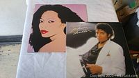 Two vinyl albums on a white sheet, one is Michael Jackson's Thriller with a black and white photo cover, the other is a Diana Ross album with a pink background and a stylized portrait of Diana Ross.
