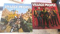 Two Village People vinyl album covers, one titled 'Cruisin'' showing band with motorcycle and bulldozer, the other showing band members in costumes on red background.