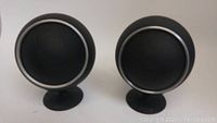 Front view of two black orb speakers with silver trim, mounted on metal stands.