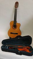 Full view of junior Española acoustic guitar standing and child violin in open case below it