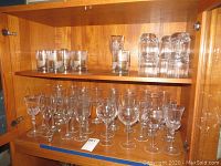 Photo showing top shelf with old-fashioned and highball glasses, bottom shelf with assorted wine glasses and one champagne flute.