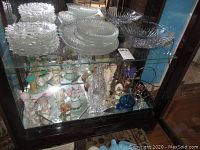 Shelf with clear textured glass saucers stacked, glass beverage decanter, and various figurines