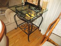 Side view showing black metal frame with scrollwork and glass top with smooth edges. Lower metal shelf visible.