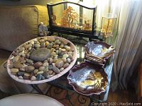 Photo displaying the glass-encased Asian art, bowl with polished rocks, and two shell-shaped dishes on a glass table