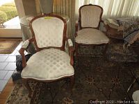 Front view of two matching vintage chairs with wooden frames and cream-colored tufted fabric seats and backs. Chairs show wear on upholstery.