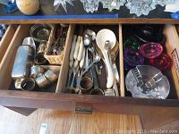 Drawer with metal salt and pepper shakers, napkin rings, stainless ladle and spoons, and small glassware.
