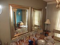 Two large matching rectangular mirrors with gold-tone frames, positioned side by side above a table with glassware.