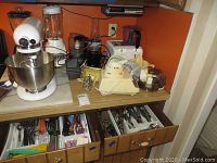 Overall kitchen counter showing KitchenAid mixer, multiple blenders, and drawers with flatware and utensils.