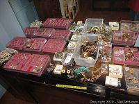 Multiple pink jewelry trays on table with assorted earrings, bracelets, necklaces and pins