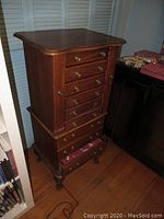 Full view of the wooden jewelry armoire showing front with drawers, side doors closed, and top surface.