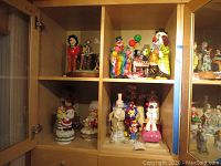 Wooden cabinet with multiple clown figurines including clowns holding balloons, a clown on a unicycle, and clown music boxes.