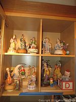 Four cubby shelves containing ceramic and paper mache clown figurines and music boxes in various styles and colors.