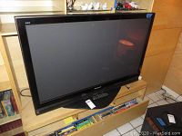 Panasonic Viera flat screen TV on a wooden entertainment unit with drawer open and other items around.