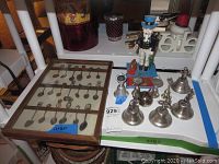 Photo showing the entire lot including Uncle Sam metal bank, set of clown bells, and wooden display case with souvenir spoons.