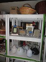 Shelves holding five teapots of different styles below, and picture frames arranged on shelf above, with baskets on top shelf