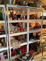Wide view of six white shelves containing various Christmas decorations including wood camels, nativity set and pillows.