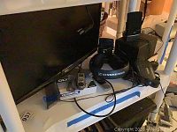 Sony Walkman on top with connected cables, black Sennheiser headphones, Olympus digital recorder, and black speakers visible on white shelf.