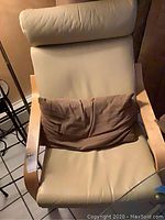 Front view of light leather chair with wooden frame and included brown pillow on seat.