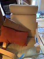 Leather chair with beige upholstery and wooden arms and base frame, including three pillows in brown and coral colors. Visible signs of wear on leather.