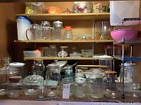 Shelving unit and cabinet with multiple glass jars, canisters, and bowls arranged across shelves, some plastic containers visible as well.
