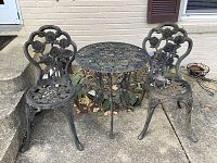 Full set showing two cast iron chairs with floral design and matching round table on concrete patio