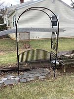 Front view of metal arched trellis with bench set against outdoor background