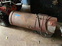 Side view of the propane bullet heater lying on the floor showing rust and overall wear.
