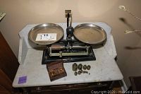 Front view of vintage torsion balance scale with two weighing pans and the black base on a marble top.