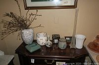 Photo showing an assortment of ceramic canisters, vases, and a wooden decorative box on a dark wood table, including willow branches in one vase.