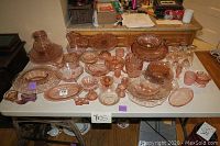 Table overview showing over 50 pieces of pink depression glass arranged with plates, bowls, stemware and serving items