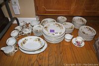 Full view of the set including cups, plates, bowls, serving dishes arranged on wooden floor.