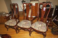 Set of 6 wooden dining chairs with floral upholstered seats on hardwood flooring. Two chairs have arms, four do not. Chairs show wear and some scratches.
