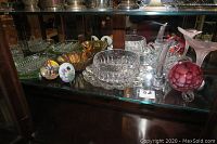 Shelf displaying clear cut glass bowls, ashtrays, platters, glass vases, pink and white swirled hummingbird feeder, and painted miniature plates.