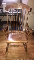 Full front view of the wooden rocking chair showing the seat, spindle back and armrests.