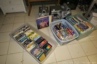 Large plastic bins filled with VHS tapes, some DVDs, and vinyl albums.