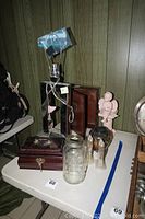 Chrome modern table lamp, wooden jewelry box, glass jar, ceramic cherub and Mexican style vase on a white table