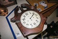 Howard Miller wooden wall clock with decorative carved top and white dial with Arabic numerals on table.