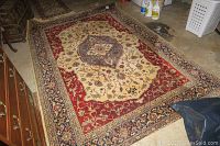 Large area rug with central medallion in cream and red tones, showing soiling and pet home wear, placed on concrete floor