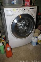 Front view of white Whirlpool Duet washer in basement with detergent containers around base