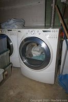 Overall view of white front-loading Whirlpool Duet Modern electric dryer in basement setting next to matching washer