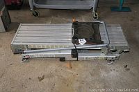 Folded aluminum ladder painters scaffold platform laid on a concrete floor showing the ribbed aluminum platform and folding frame with locking components.