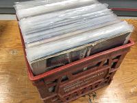 Red plastic Dominion Dairies Ltd milk crate filled with vinyl records in clear protective sleeves placed on wooden surface
