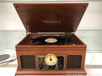 Open top view of mahogany Victrola turntable with black vinyl record on platter, raised lid showing inner turntable area