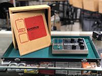 Three-quarter view of pedal on green surface with wooden display behind