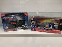 Photo of two Transformers Armada toys in original packaging, one a blue/gray car transport truck, the other a green weaponized vehicle.